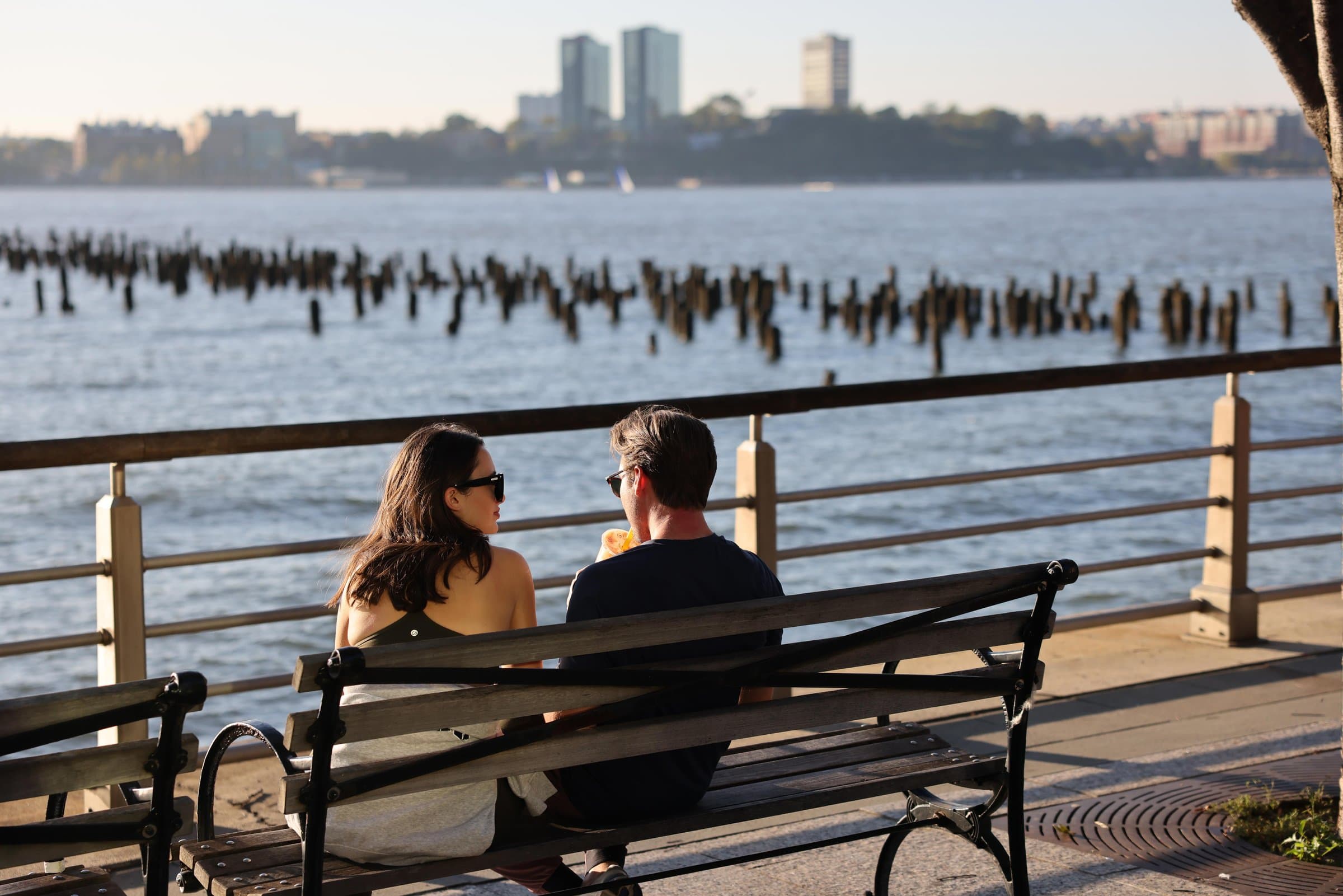 Two people sitting on a bench beside water and wooden pilings